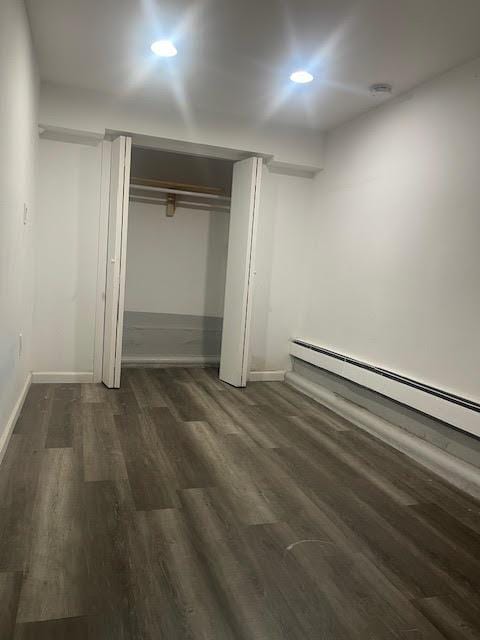 unfurnished bedroom featuring a closet, a baseboard heating unit, baseboards, and wood finished floors