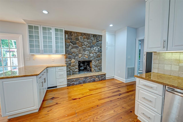 kitchen with light wood-style flooring, a fireplace, visible vents, white cabinets, and backsplash