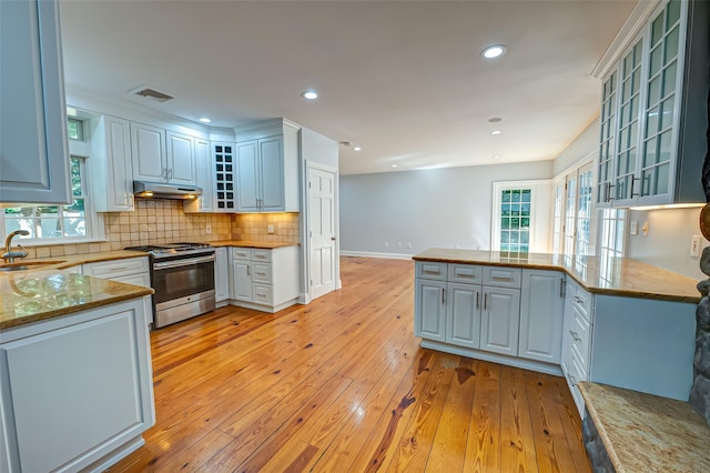 kitchen featuring visible vents, light wood-style flooring, decorative backsplash, stainless steel gas range, and under cabinet range hood