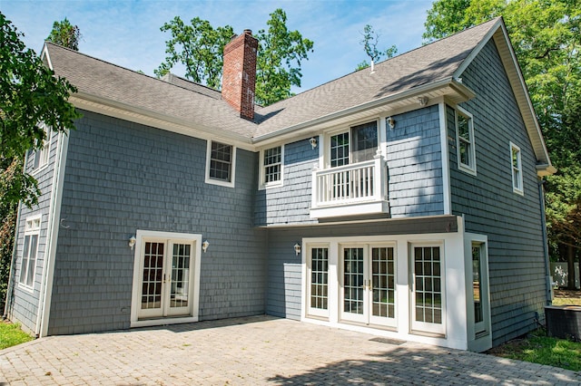 back of property with french doors, a patio area, a chimney, and a balcony