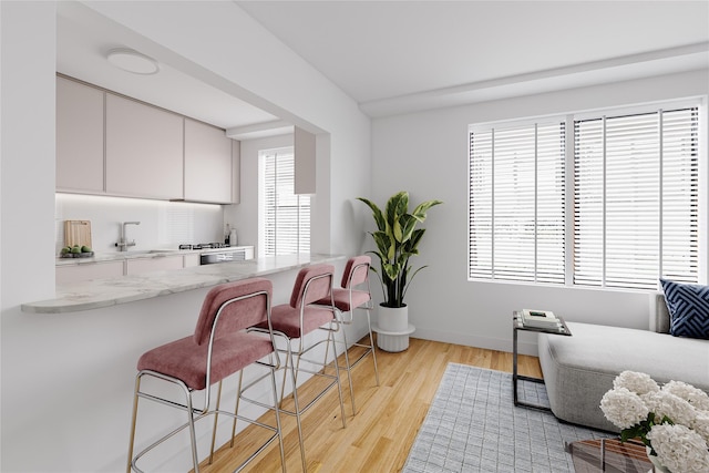 interior space featuring white cabinets, light stone counters, a breakfast bar, light wood-type flooring, and a sink