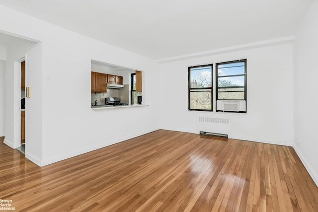 unfurnished living room featuring radiator heating unit, cooling unit, light wood-style flooring, and baseboards