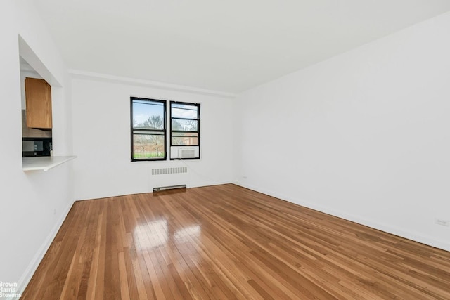 unfurnished room featuring radiator, baseboards, and light wood finished floors