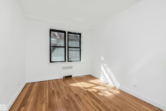 empty room featuring baseboards, light wood-style floors, and radiator