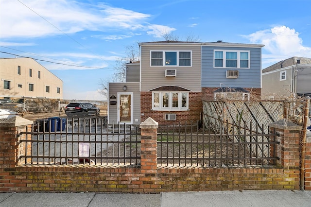 view of front facade featuring brick siding, a fenced front yard, a wall mounted AC, and a gate