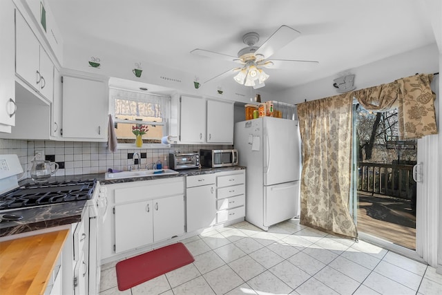 kitchen featuring gas range oven, stainless steel microwave, freestanding refrigerator, white cabinetry, and a sink