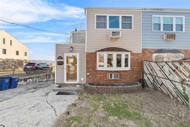 view of front of house featuring fence, an AC wall unit, and brick siding