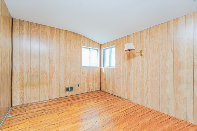 empty room with hardwood / wood-style flooring, visible vents, lofted ceiling, and wood walls