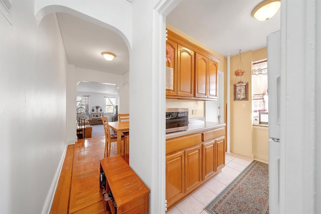 interior space featuring light tile patterned floors, baseboards, arched walkways, light countertops, and stainless steel microwave