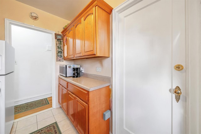 kitchen with light countertops, stainless steel microwave, light tile patterned flooring, and freestanding refrigerator