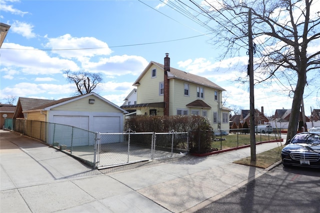 view of side of property with an outbuilding, a fenced front yard, a detached garage, a gate, and a chimney