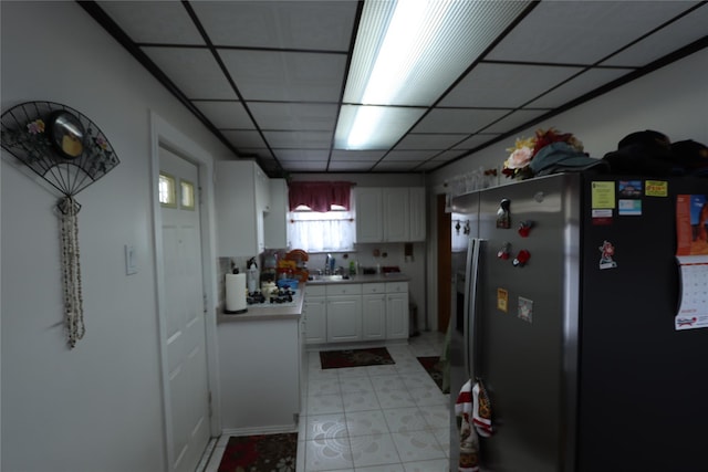 kitchen with light countertops, a drop ceiling, white cabinetry, a sink, and stainless steel fridge