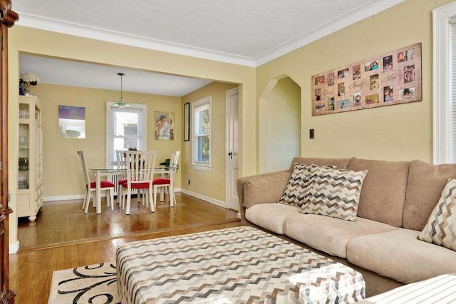 living area with arched walkways, crown molding, baseboards, and wood finished floors