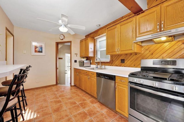 kitchen featuring light countertops, appliances with stainless steel finishes, light tile patterned flooring, a sink, and under cabinet range hood