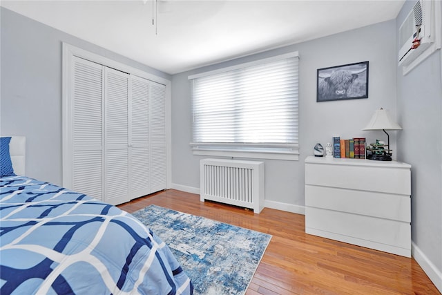 bedroom featuring light wood-type flooring, radiator heating unit, baseboards, and an AC wall unit