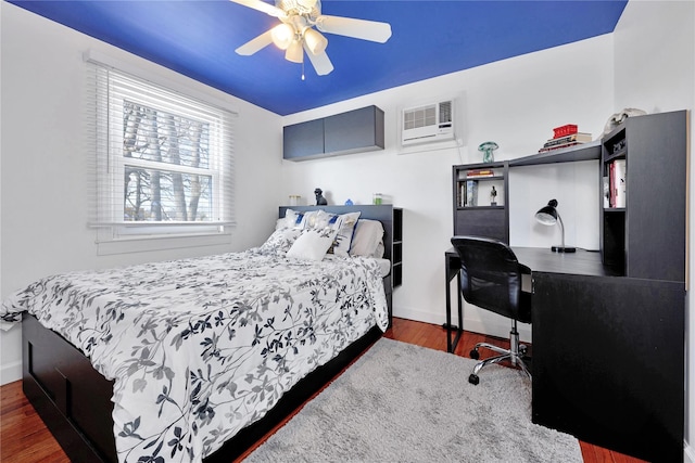 bedroom with ceiling fan, baseboards, an AC wall unit, and wood finished floors