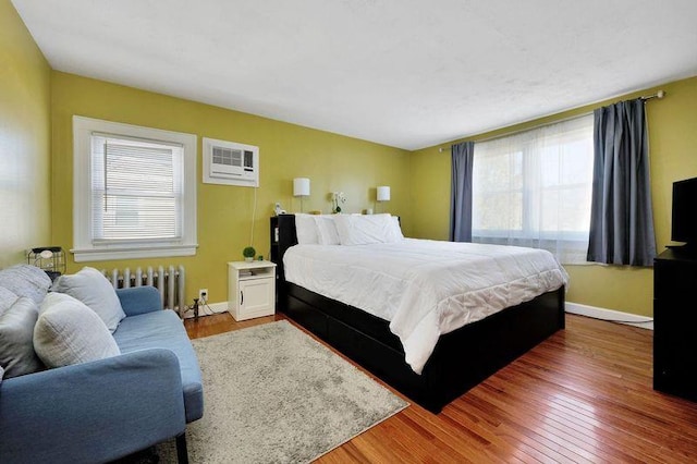 bedroom featuring an AC wall unit, multiple windows, hardwood / wood-style floors, and radiator heating unit