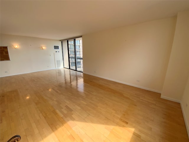 empty room featuring a wall of windows, baseboards, visible vents, and light wood finished floors