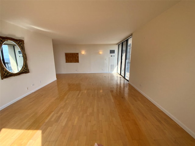 unfurnished room with light wood-type flooring, expansive windows, and baseboards