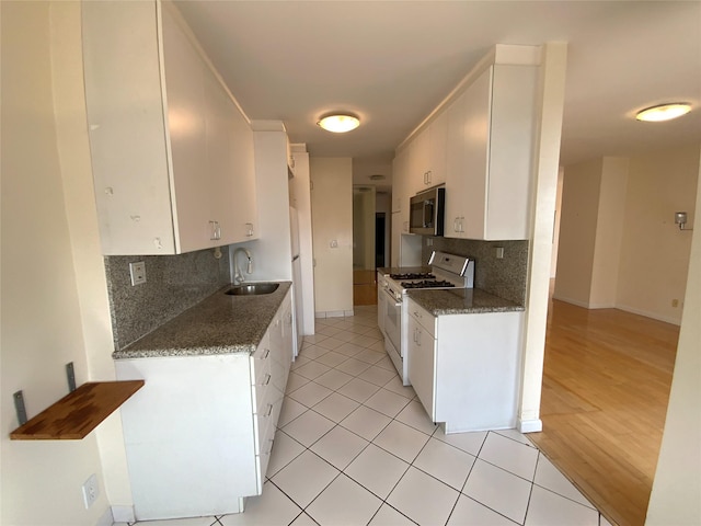 kitchen with white gas stove, tasteful backsplash, stainless steel microwave, white cabinetry, and a sink