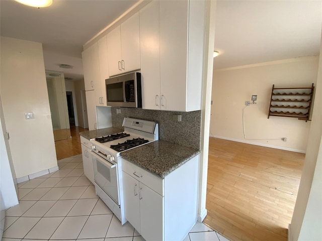 kitchen with white range with gas stovetop, white cabinets, ornamental molding, backsplash, and stainless steel microwave