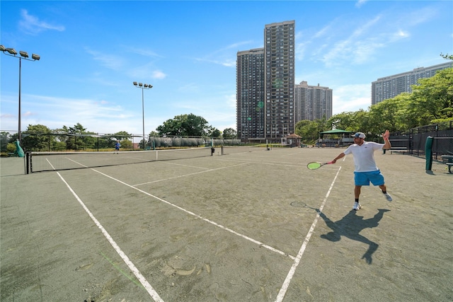 view of tennis court featuring a city view and fence