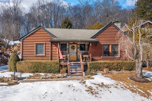 log cabin with log siding, roof with shingles, covered porch, and a chimney