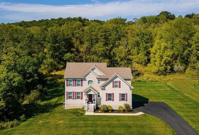 colonial home featuring driveway, a view of trees, and a front lawn