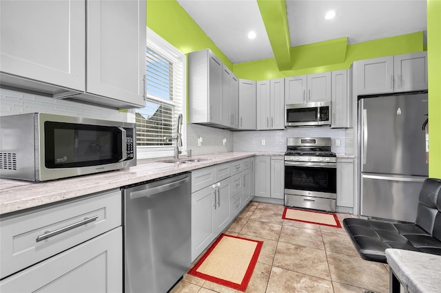 kitchen with light tile patterned floors, backsplash, appliances with stainless steel finishes, a sink, and light stone countertops