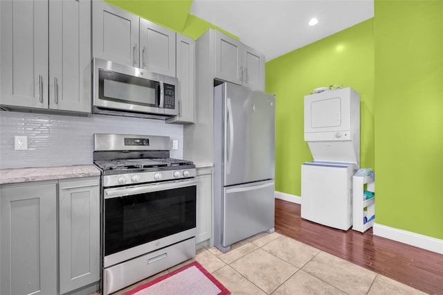 kitchen with stacked washer and dryer, appliances with stainless steel finishes, backsplash, and gray cabinetry