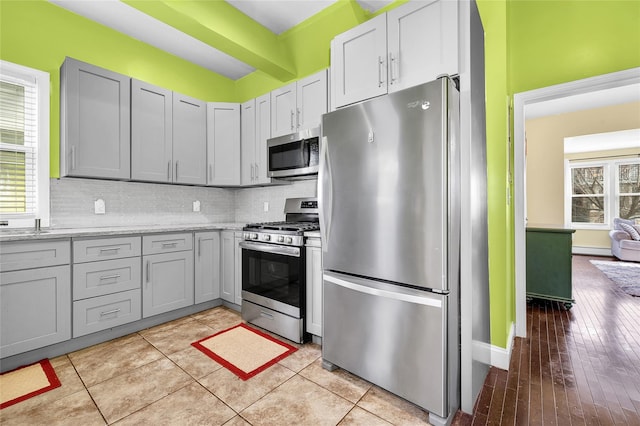 kitchen with tasteful backsplash, appliances with stainless steel finishes, light stone counters, and gray cabinetry