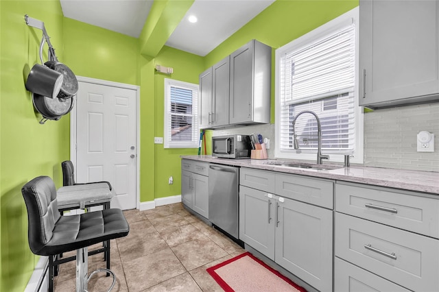 kitchen featuring light tile patterned floors, stainless steel appliances, a sink, baseboards, and backsplash