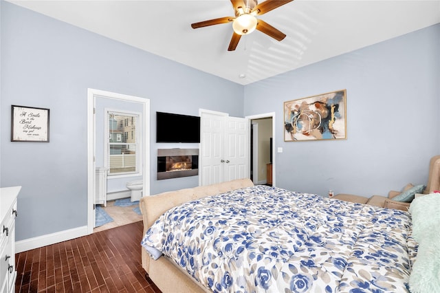 bedroom featuring ensuite bathroom, dark wood-type flooring, a glass covered fireplace, a baseboard heating unit, and baseboards