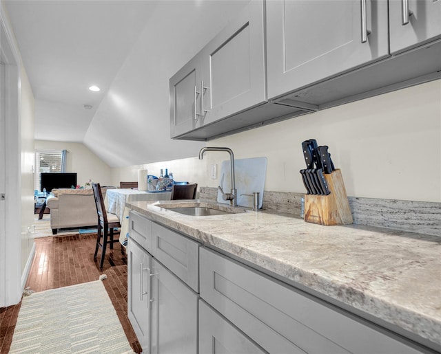 kitchen with a sink, vaulted ceiling, open floor plan, light stone countertops, and dark wood-style floors