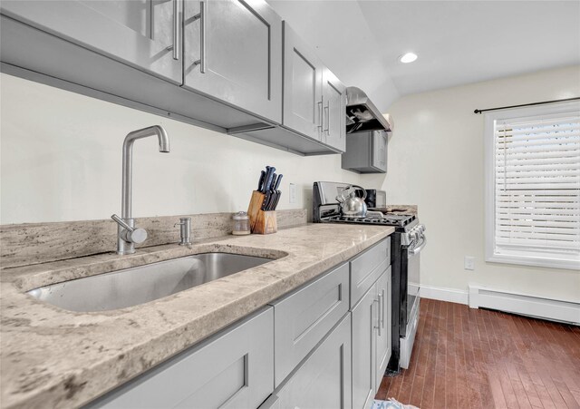 kitchen featuring stainless steel gas range oven, dark wood-style flooring, a sink, baseboards, and wall chimney range hood