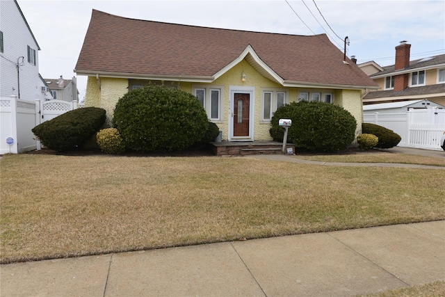 view of front of home featuring a front lawn, a shingled roof, fence, and a gate