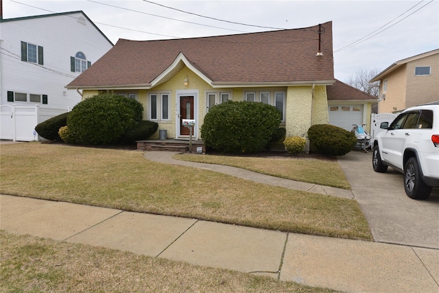 view of front facade with a garage, fence, concrete driveway, roof with shingles, and a front yard