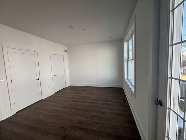 unfurnished bedroom with dark wood-style floors, visible vents, and baseboards