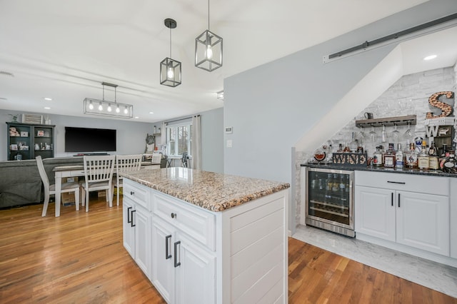 kitchen with white cabinets, wine cooler, decorative light fixtures, light stone countertops, and light wood-type flooring