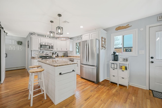 kitchen featuring a center island, visible vents, light wood-style flooring, decorative backsplash, and appliances with stainless steel finishes