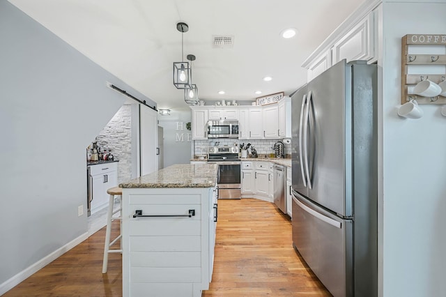 kitchen featuring a barn door, stainless steel appliances, backsplash, and light wood-style flooring