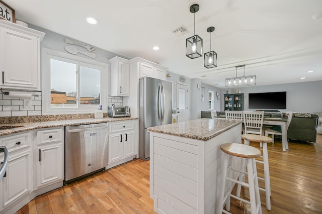 kitchen featuring stainless steel appliances, a kitchen island, visible vents, light wood-style floors, and white cabinetry