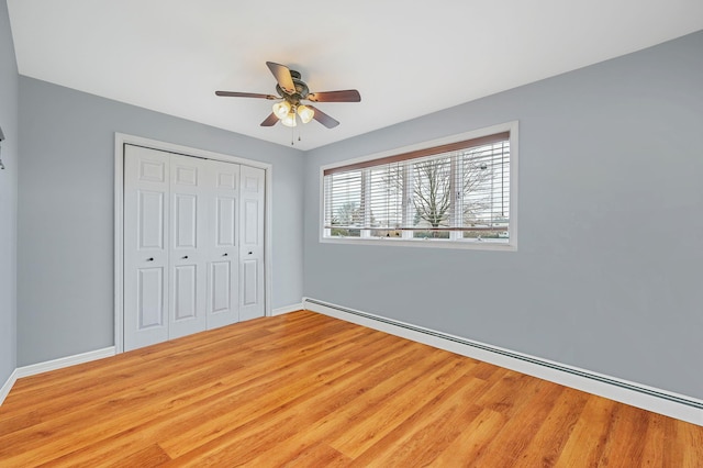 unfurnished bedroom with baseboards, a ceiling fan, wood finished floors, a baseboard heating unit, and a closet