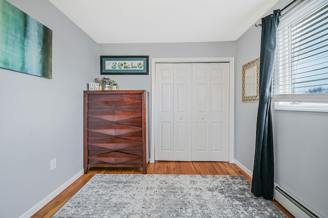 bedroom with a baseboard radiator, a closet, baseboards, and wood finished floors