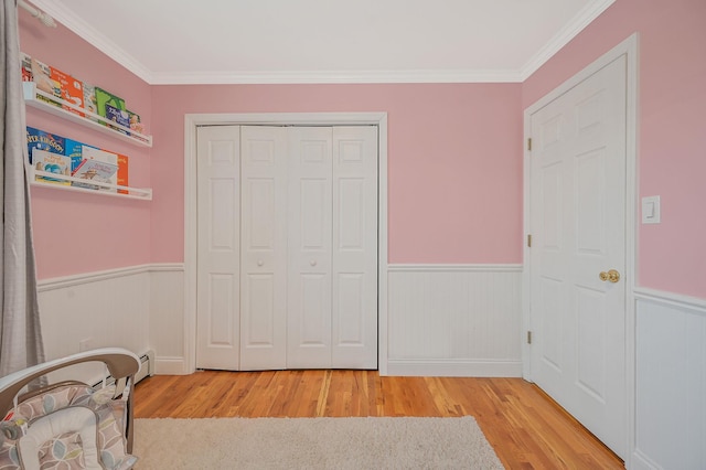 bedroom with light wood-style floors, a closet, wainscoting, and ornamental molding