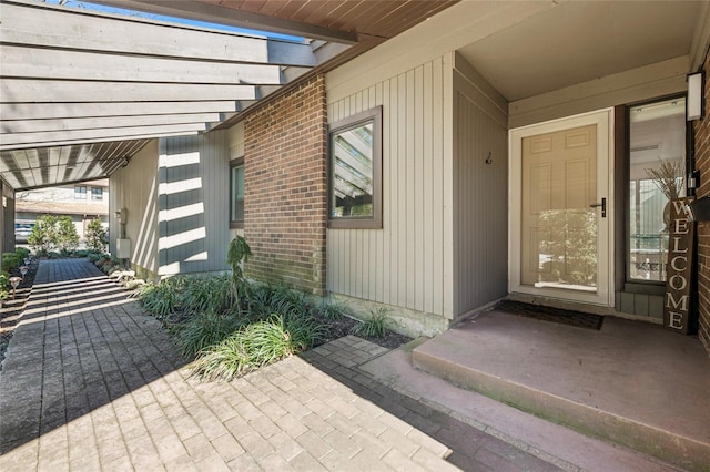 view of exterior entry with brick siding and a pergola