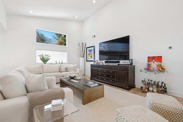 living room with visible vents, baseboards, a high ceiling, recessed lighting, and light wood-type flooring