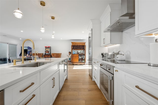 kitchen featuring decorative light fixtures, wall chimney range hood, white cabinetry, stainless steel appliances, and light wood finished floors