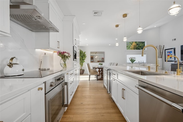 kitchen with visible vents, a sink, stainless steel appliances, white cabinets, and wall chimney range hood