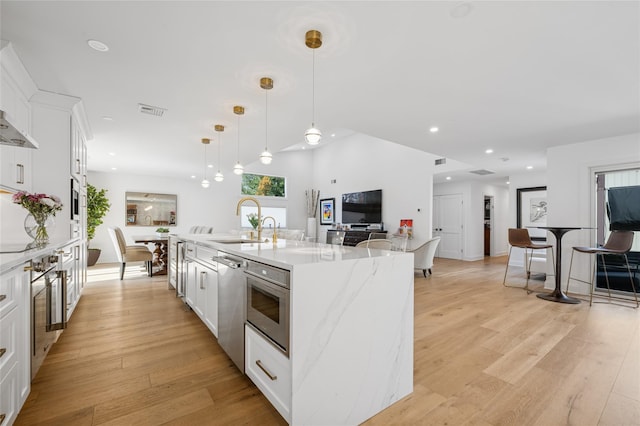 kitchen with a sink, a large island, white cabinets, light wood-style floors, and stainless steel dishwasher